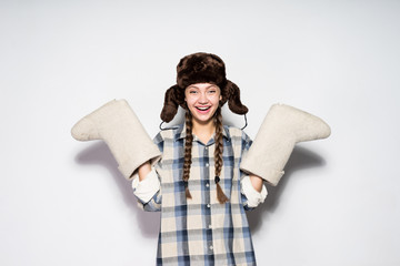 happy beautiful Russian girl in a cap with ear-flaps holds warm gray felt boots, laughs