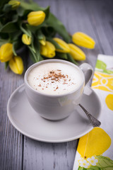 Coffee cappuccino with ceylon cinnamon and yellow tulips on a gray background