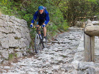 Radfahrer mit blauer Jacke von vorne auf holprigen Weg