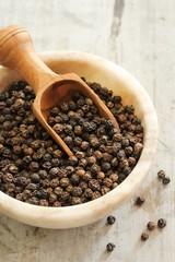 Whole Black Pepper in a bowl with wooden scoop, selective focus