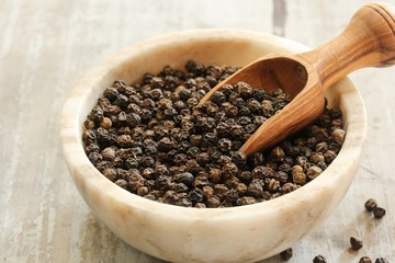 Whole Black Pepper in a bowl with wooden scoop, selective focus