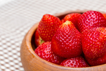 The fresh strawberries in the woonden bowl on the mat. 