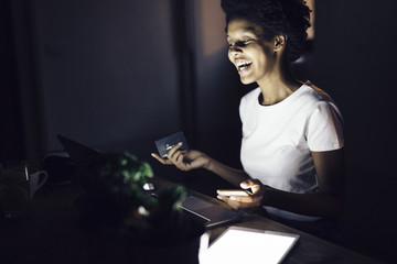 Young woman with credit card, shopping online at night from home