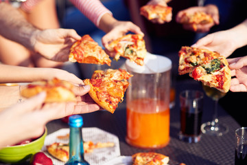 Close up of pizza pieces in hands of friends
