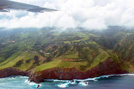 Aerial view of Maui's coastline shows everything from Pacific surf to rocky cliffs to green meadows to mountains to clouds and the wing of a small airplane