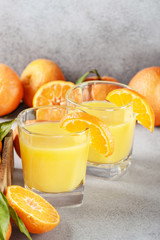 Fresh orange tangerines with green leaves and juice glass on table
