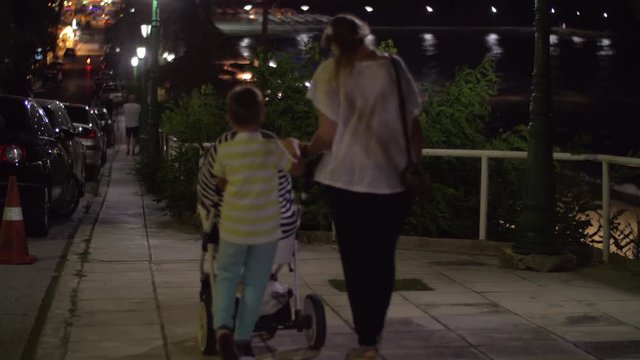 Mother and children walking in the street late in the evening. Elder son helps to push pram