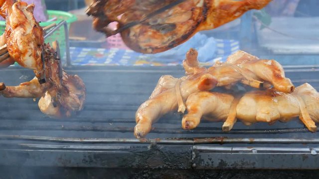 Whole chicken carcass grill strung on wooden stick grilling on the grill. Street Food Thailand. Men's hands turn over the grilled chicken