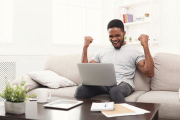 Young black man with raised arms, with laptop celebrating success