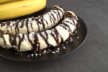 Bananas with chocolate and coconut chips on grey background.