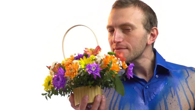 A stylish man in blue bodyart sniffs a basket of flowers, slow motion