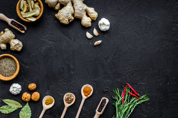 Condiments, seasoning and spices concept. Dry spices in wooden spoons near ginger, rosemary, chili pepper on black background top view copy space
