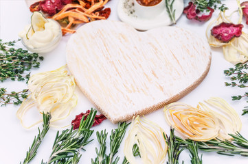 Homemade colorful chips of different fresh vegetables - beets, sweet potatoes, carrots, cucumber, onions, rosemary and thyme on a light background around the white Board in the shape of a heart.