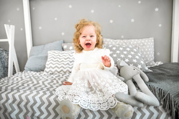 Fototapeta premium little girl is sitting on the bed with her toy