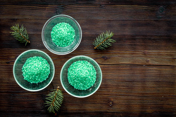 Spa cosmetics. Green spa salt with pine scent on dark wooden background top view copy space