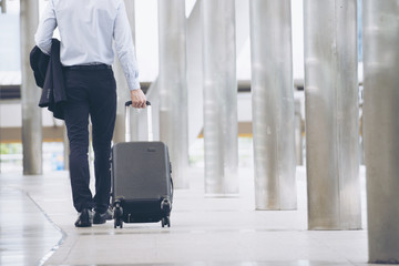 Businessman Dragging suitcase luggage,walking to passenger boarding in Airport.Asian tourist men wearing black suit with trolley bag.