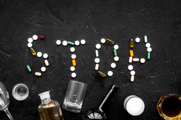 Obraz premium Stop alcohol. Word stop lined with pills near glasses and bottles on black background top view copy space