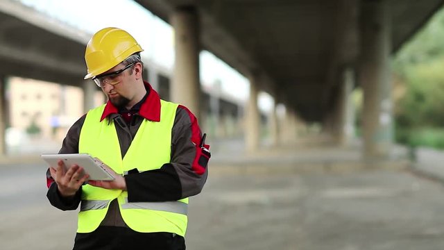 Workman with tablet computer under overpass. Manager of repair works at construction site under overhead road, inputs data in computer