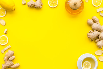 Warming tea with lemon and ginger. Cup, teapot, ginger root on yellow background top view copy space