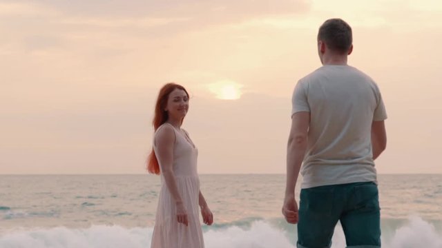 young couple admiring the sunset on the ocean shore, back side, slow motion