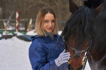 Portrait of a young girl with white hair next to a brown horse. The girl holds the horse and...