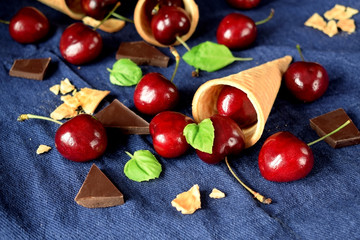 Waffle cones, cherries and chocolate on blue background. Ingredients for a dessert cooking