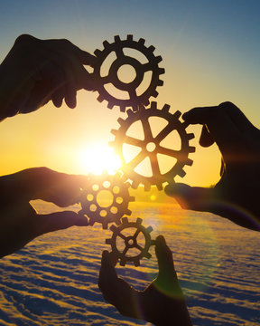four hands of businessmen trying to connect the gear from the gears of the details of the puzzles. against the background of sunlight. Concept business idea. Teamwork, strategy, cooperation