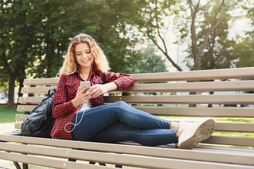 Beautiful woman sitting and listening to music on the smartphone outdoors