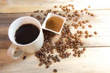 A cup of coffee with small white ceramic dish full of ground coffee and coffee beans on wooden background, Top view