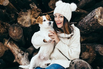 .Sweet and pretty girl sitting on a wooden log playing with her nice dog jack russell outdoors in...