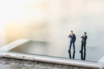 Business and communication Concept. Two businessman miniature figures standing on smart phone.