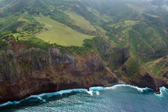 Aerial view of green meadows and rocky cliffs on the coast of the island of Maui in Hawaii, shot from a small, low-flying prop plane