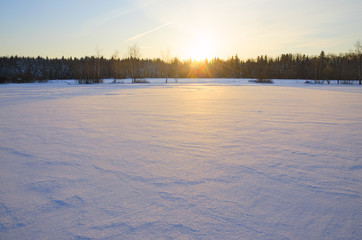 Frosty winter landscape with rising sun.Snowy background.Crisp snow on the surface of frozen lake.Cold morning.