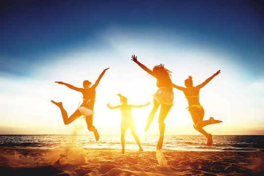 Four happy girls run and jump against sunset sea