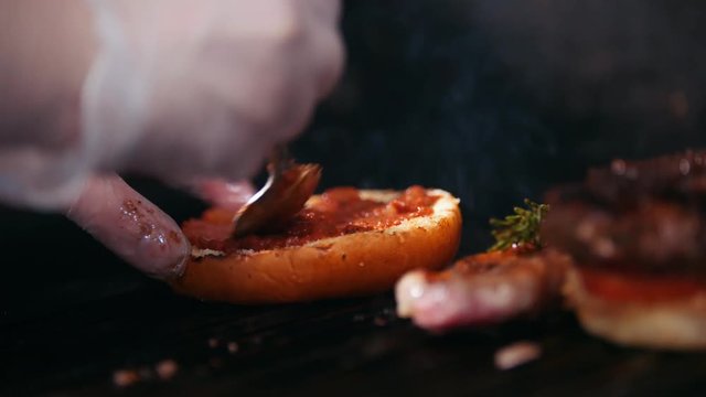 Chef preparing the burger, frying the bun on the grill, putting the tomatoes, meat and sauce