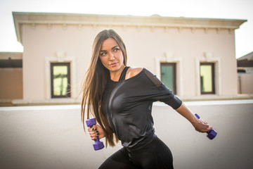 Portrait of beautiful fitness girl with dumbbells outdoors.