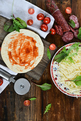 Ingredients for Pizza: basis dough, salami sausage, cherry tomatoes, grated cheese, tomato paste, herbs and arugula. Natural Wooden Background With Linen Napkin and Knife For Pizza