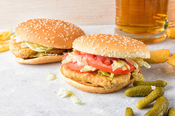 Chicken burger and glass of beer. Homemade hamburgers, pickles and chips  on wooden tray. White marble background. 