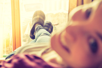 Junge Frau liegt gemütlich auf Couch, Gesicht in der Unschärfe, lächelnd