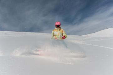 Fototapeta na wymiar Female snowboarder in pink helmet and glasses riding down the mountain slope