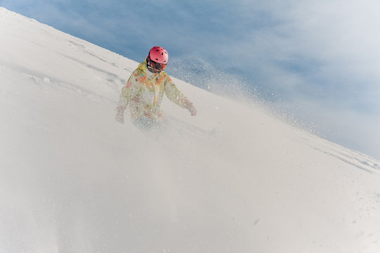Female snowboarder in colorful sportswear and pink helmet riding down the snow hill