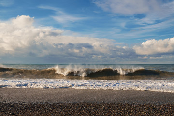 Long wave on a stony beach, blue cloudy sky background