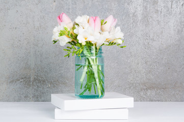 fressia and tulip flowers in a blue glass jar