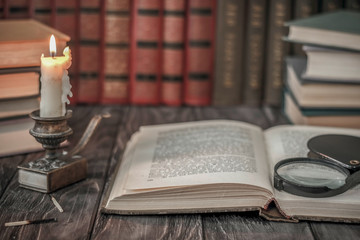 Naklejka premium On the wooden background of the table there are stacks of colorful books near the old candlestick with burnt matches lying next to each other.