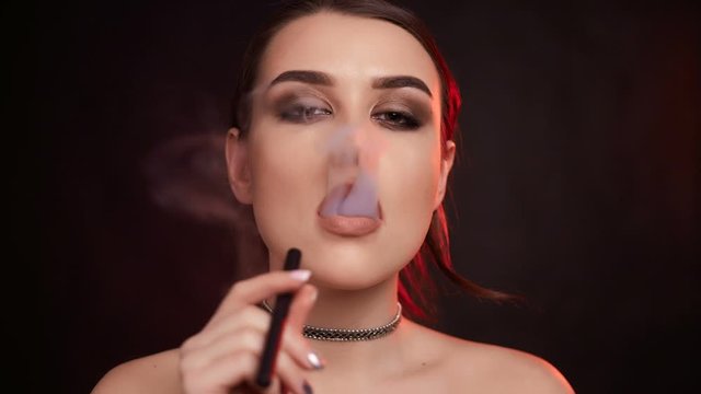Slow motion portrait of glamour seductive gorgeous brunette woman smoking electronic cigarette in studio