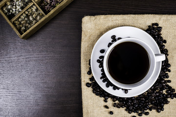 Black coffee in white cup and coffee bean and box on cloth and wood background.