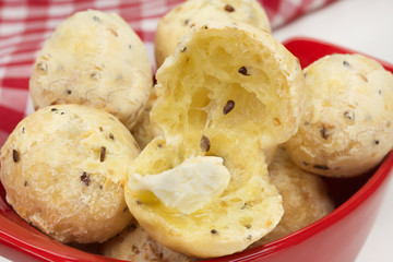 Traditional Brazilian snack cheese bread in multigrain version in a red bowl close with one cut with butter