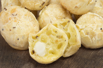Traditional Brazilian snack cheese bread in multigrain version in wood background close with one cut with butter