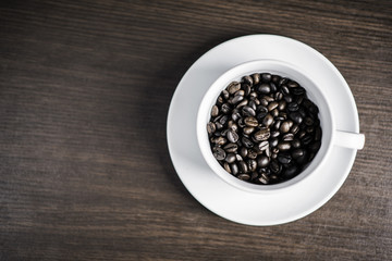 Coffee bean in white cup on wood background.