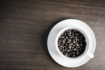 Coffee bean in white cup on wood background.